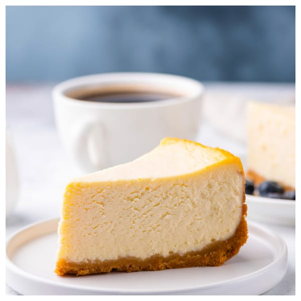 A slice of Davinci's classic Italian cheesecake with a coffee cup in the background.