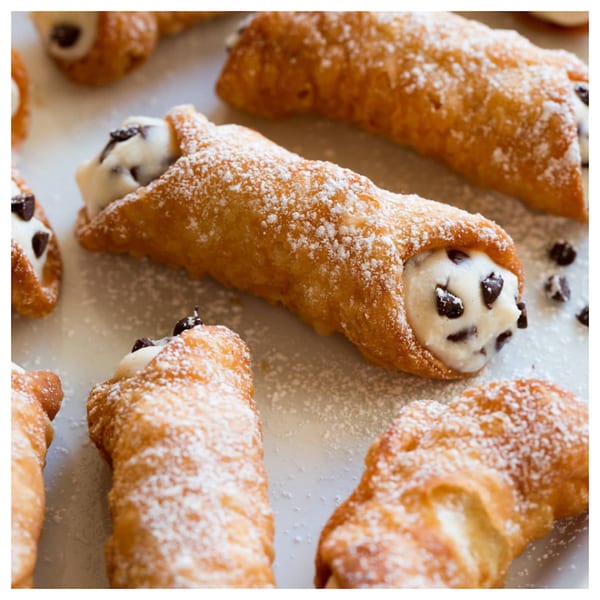 Several Davinci's cannolis, filled with cream and chocolate chips, dusted with powdered sugar.