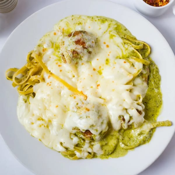 Davinci's pesto pasta with meatballs and melted mozzarella cheese on a white plate.